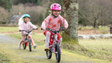 Two children riding kids bikes on a path in a park.