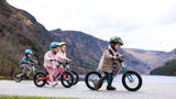 Children riding balance bikes on a path with mountains in the background