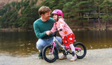Simon teaching a young girl how to ride a bike by a lake